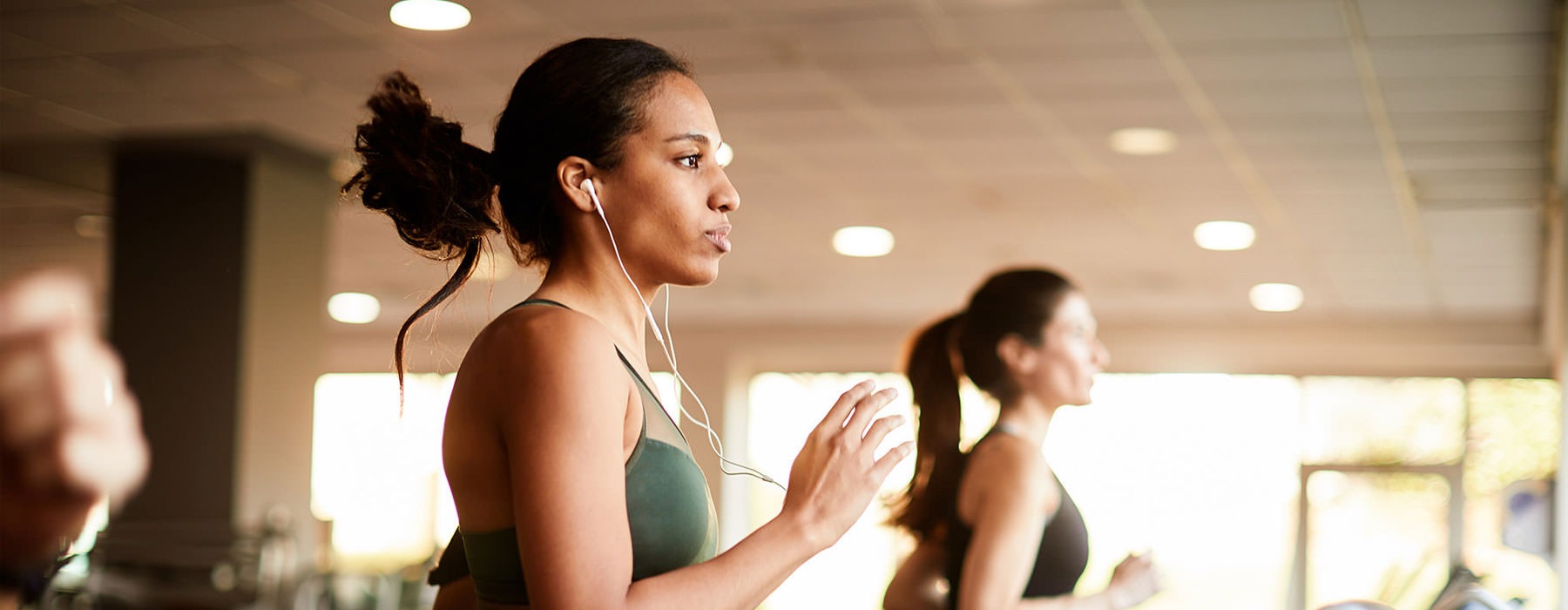 Young woman running on treadmill, wearing earphones